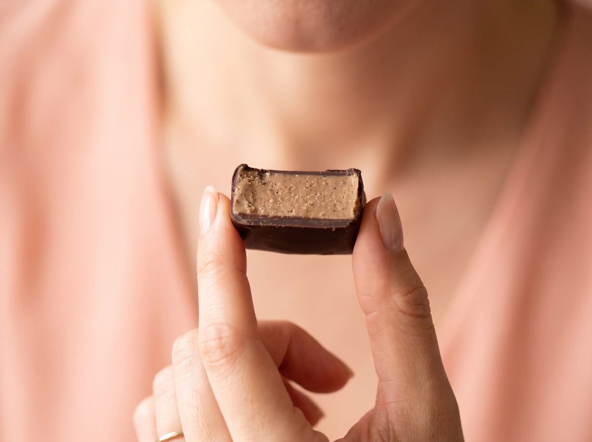 Une femme tient entre ses doigts une bouchée de chocolat noir CacaoCare